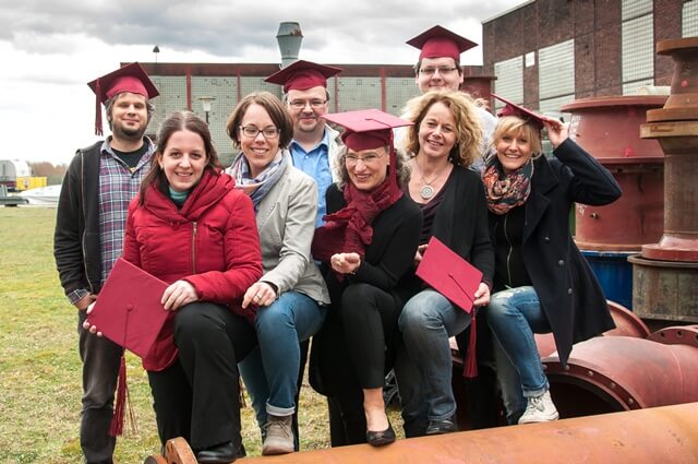 Die acht Alumni Cross Media Redakteur (IHK) lächeln glücklich in die Kamera