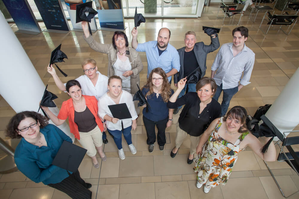 Die 11 Teilnehmer der Abschlussveranstaltung der Fortbildung stehen am Fuß der Treppe und winken in die Kamera